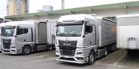Eigener Fuhrpark: zwei silberne LKW mit Auflieger der Firma Herholz an einer Laderampe.