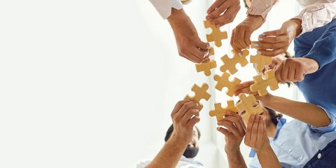 Gruppe von Menschen hält Puzzleteile in die Mitte.