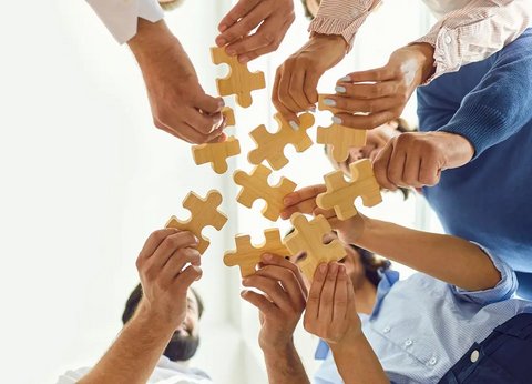 Gruppe von Menschen hält Puzzleteile in die Mitte.